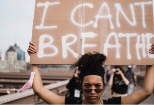 Μία γυναίκα διαδηλώνει κρατώντας ένα χαρτόνι το οποίο γράφει "I Can't Breathe"